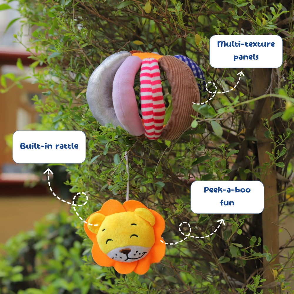 Plush lion toy with multi-texture panels and built-in rattle, hanging from a tree.
