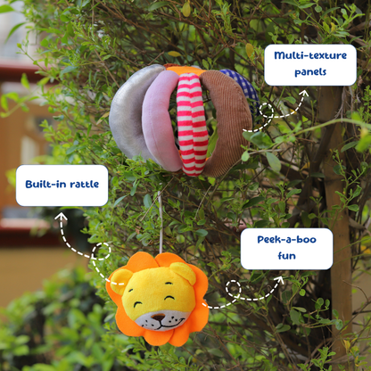 Plush lion toy with multi-texture panels and built-in rattle, hanging from a tree.