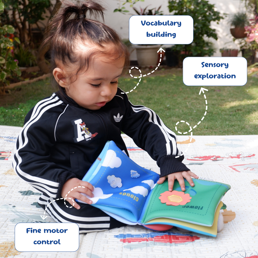 Child playing with a soft book outdoors, with text labels on vocabulary building, sensory exploration, and fine motor control.